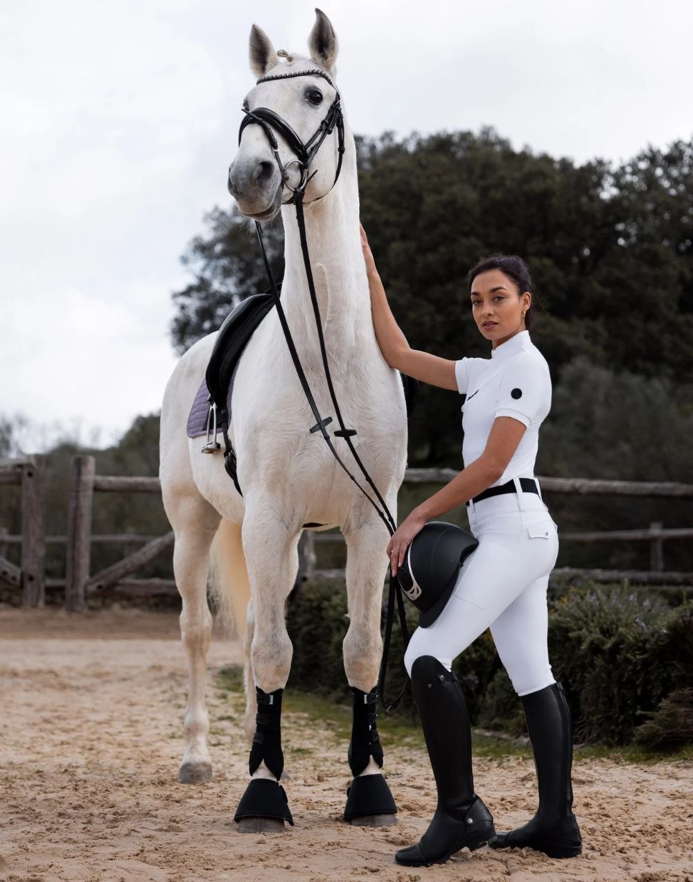 Rider in tall black boots beside a grey horse